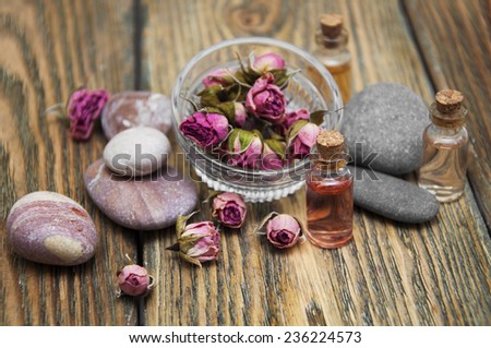 Aromatic essences in small bottles and dry roses in bowl on wooden background