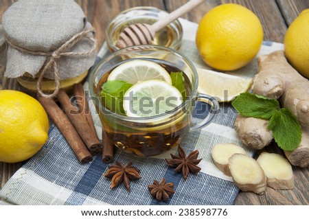 A cup of tea with fresh honey, lemon, ginger and spices on wooden background