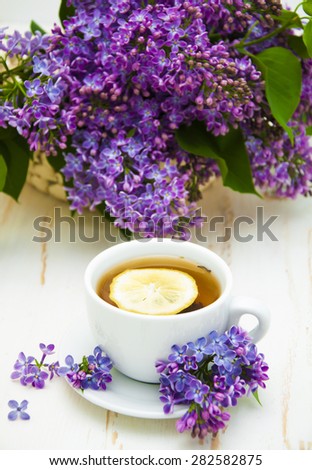 A cup of tea with a bouquet of lilacs on a wooden background