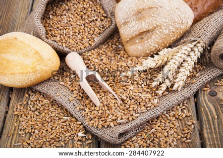 wheat grain in a small bag and different bread on a wooden background