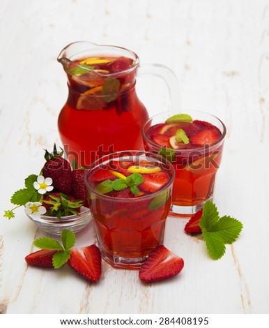 Cold strawberry drink with fresh strawberries and lemon on white wooden background