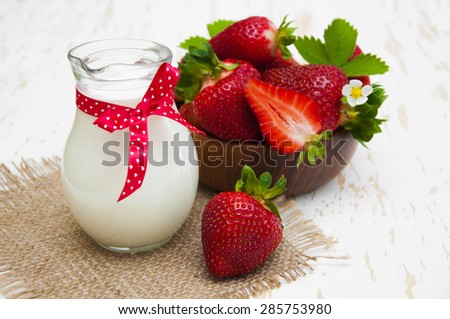 Fresh milk in a jug with fresh strawberries on a napkin on wooden background