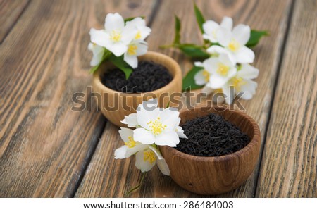 Dry black jasmine tea with jasmine flowers in wooden bowls on a wooden background