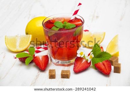 Cold strawberry drink with fresh strawberries and lemon on white wooden background