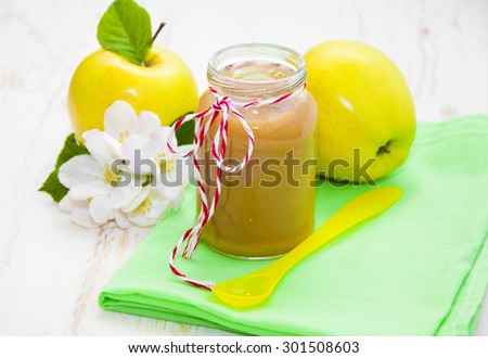 Baby apple puree in a jar with apples and blossom on wooden white background