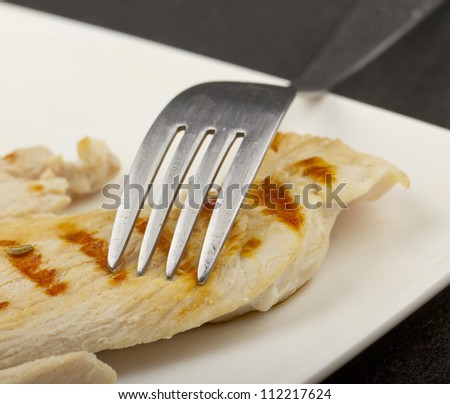 Piece of grilled meat with fork, over white plate
