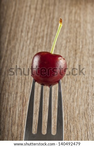 Single red cherry stuck on the prongs of a fork
