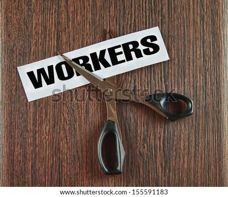 Scissors cutting the word workers written on a paper strip, over wooden background