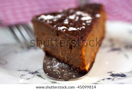 Piece of cake (pumpkin and pine, with icing sugar) on silver cutlery, white plate and red and white tablecloth