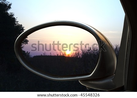 Sunset on a field, reflected in the rear-view mirror of a car