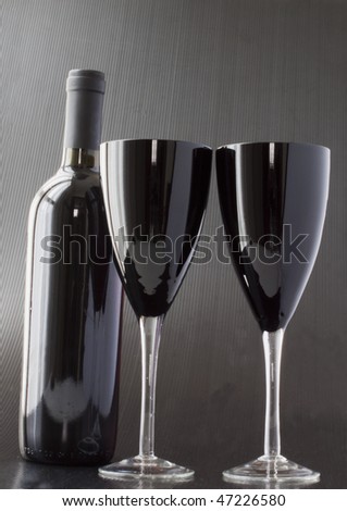 Two black glasses for wine over black background, with a black wine bottle