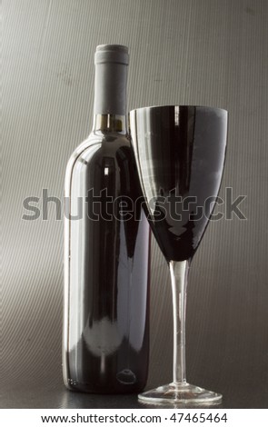 A black glass for wine over black background, with a black wine bottle