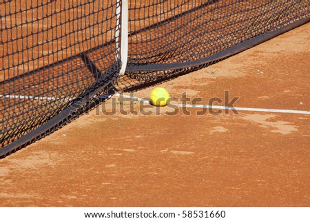 A yellow tennis ball near the net on a clay court