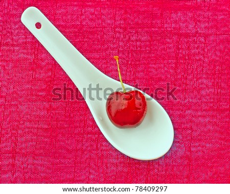 Single cherry over a white spoon, over red cloth