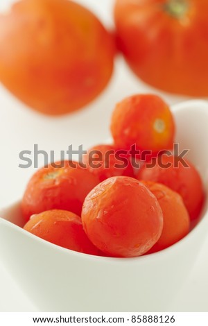 Close up of little tomatoes in a white cup, with big tomatoes on the back