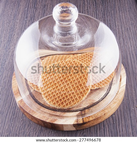 Round waffels under bell jar, over wooden table, horizontal image