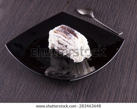 Slice of ice cream cake over black plate, wooden table, horizontal image