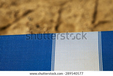 Deckchair in strict closeup, with sand of beach on the background, horizontal image