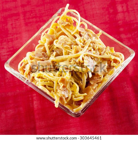 Pasta with ham and eggs in square galls plate, red cloth, square image