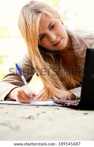 beautiful student girl with laptop in the park, taking notes