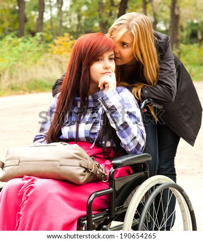 teen girl on the wheelchair with her friend in the park