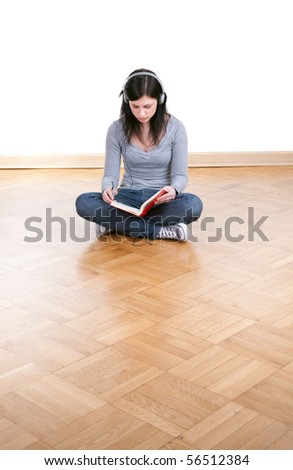 young woman in headphones reading book, sitting on the floor with crossed legs