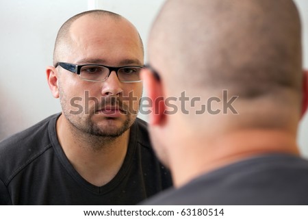 sad man in glasses looks in mirror