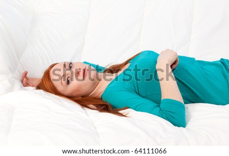 beautiful young woman in turquoise blouse lying on white bedding