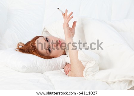 smoking beautiful young woman relaxing in white bedding