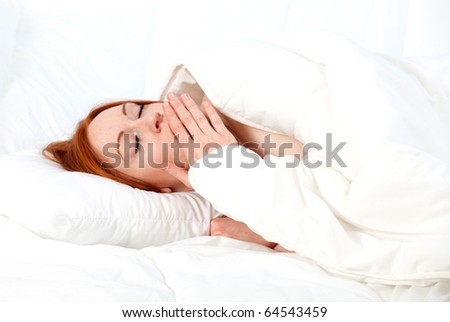 yawning beautiful young woman relaxing in white bedding