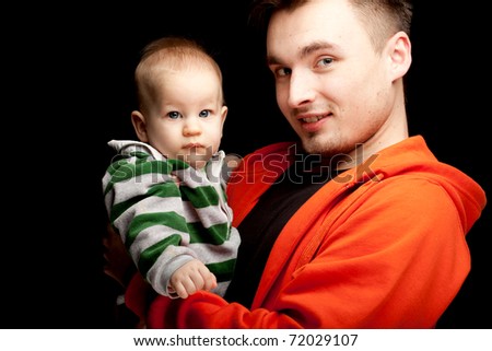 portrait of young father holding its lovely six months old son, black background