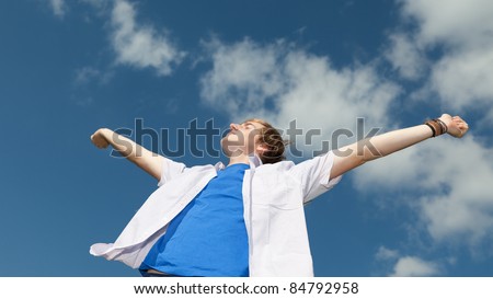 portrait of a happy young man with arms outstretched against sky