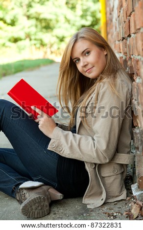 young woman reading or studying book outdoors leaning on the old bricks wall