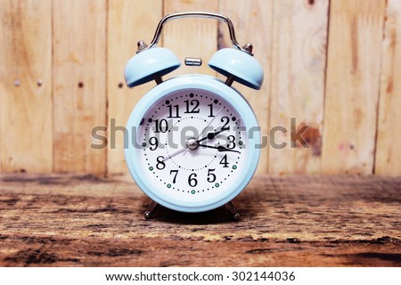 Retro alarm clock on the old wood background in vintage pastel tones.