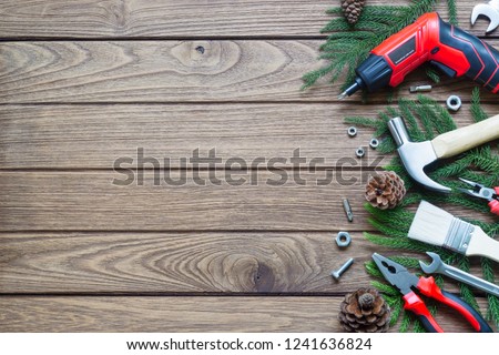 Merry Christmas and Happy new year handy construction tools background concept. Hammer, wrenches, screwdriver, pliers, paint brush, pine leaves, pine cones decoration on wood background. Top view with