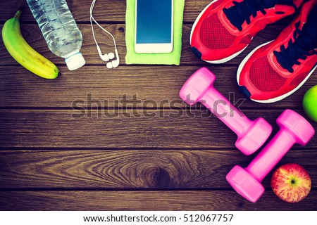 Fitness, healthy and active lifestyles Concept, dumbbells, sport shoes, bottle of waters, smartphone with headphone, banana and apples on wood background. copy space for text. Top view