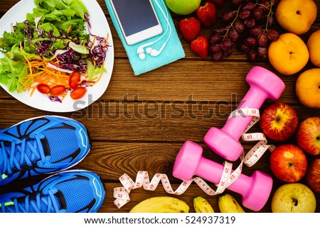 Fitness, healthy fruits, Fresh healthy salad, diet and active lifestyles Concept, dumbbells, Fresh healthy salad, fresh fruits, sport shoes, smart phone on wood background. copy space for text.