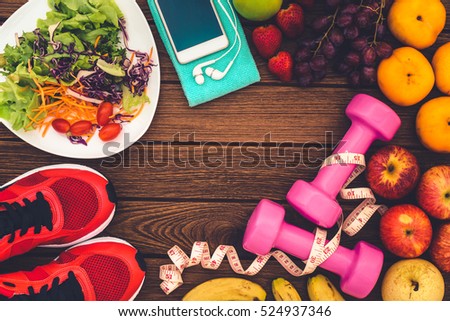 Fitness, healthy fruits, Fresh healthy salad, diet and active lifestyles Concept, dumbbells, Fresh healthy salad, fresh fruits, sport shoes, smart phone on wood background. copy space for text.