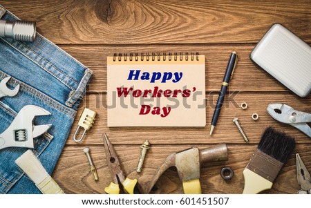 Workers' day background concept - Jeans, many handy tools, notebook with happy workers' day text , wooden background top view