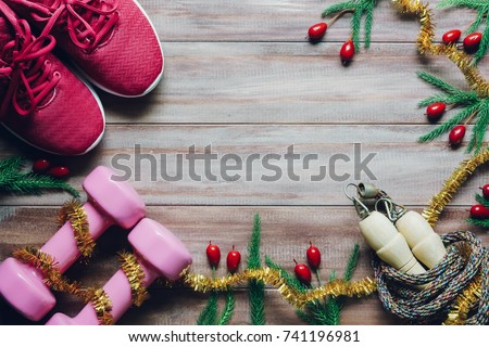 Fitness, healthy and active lifestyles greeting card concept, dumbbell, sport shoes, skipping rope or jump rope with Christmas decoration on wood background Merry Christmas and Happy new year concept.