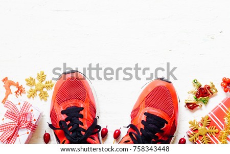 Pair of red sport shoes with Christmas decoration items and presents boxes laid on grunge white wooden floor background, top view with copy space