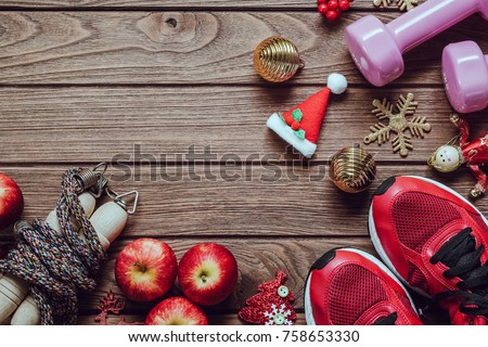 Fitness, healthy and active lifestyles love concept, dumbbells, sport shoes, skipping rope or jump rope and apples with Christmas decoration items on wood background.