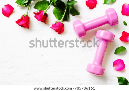 Pink sport dumbbells,  and red roses on white wooden background, Valentines sports background and greeting card any anniversary holiday background concept top view with copy space.