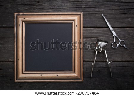 Barber equipment, scissors, vintage clipper and black sheet in a wooden frame on a black wooden background