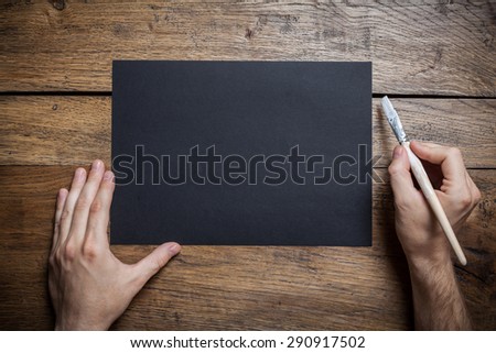 Men\'s hands with brush, white paint and black sheet on vintage wooden background with place for text