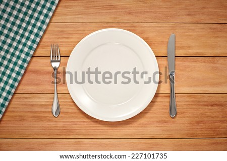 Empty Plate, Fork, Knife and Table Cloth on wooden background. Top View with Text Space
