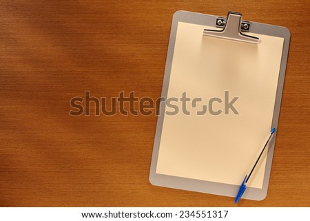 Clipboard with Blank Paper and Blue Pen on Wooden Table. Top View of Desk with Copy space for text or image