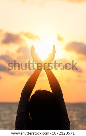 Summer sun June solstice concept and silhouette of happy young woman\'s hands relaxing, meditating and holding sunset against warm golden hour sky on the beach with ocean or sea background
