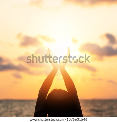 June summer sun solstice concept with silhouette of happy young woman\'s hands relaxing, meditating and holding sunset against warm golden hour sky on the beach with natural ocean or sea background