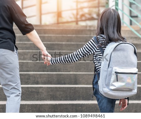Educational back to school or bring kid to work concept with elementary student girl carrying backpack holding parent woman or mother\'s hand walking up school admission office building going to class